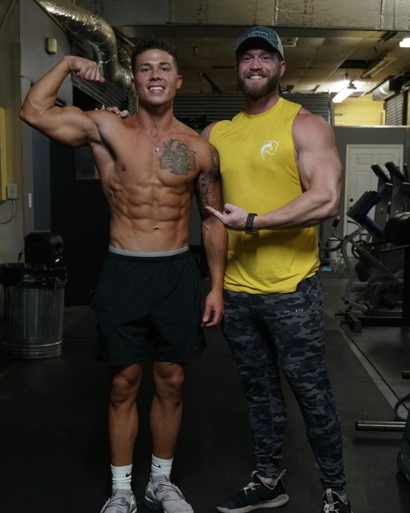 The coach points at a client flexing his bicep in the gym.