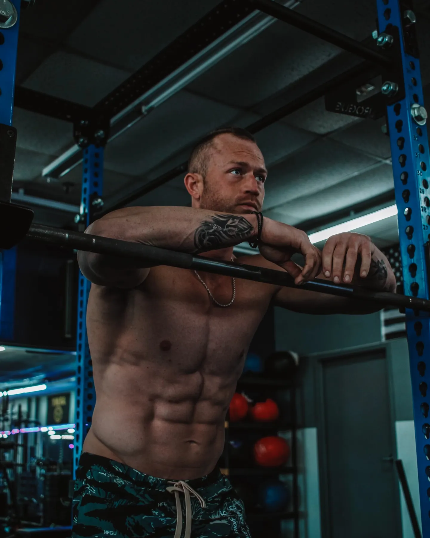 The coach rests his arms on a barbell in a squat rack.